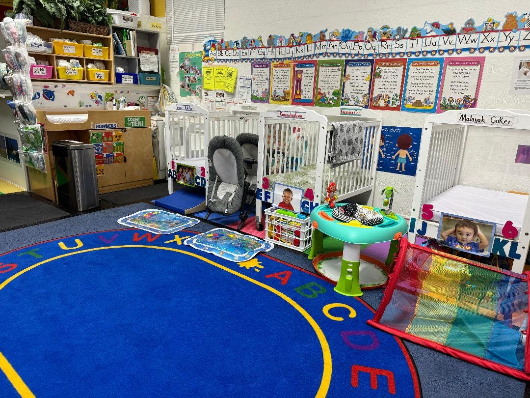 Daycare room with cribs, playmats, and a blue alphabet rug