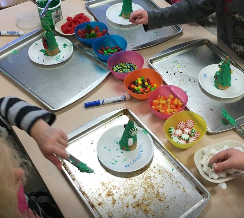 People decorating green cone-shaped cookies with candy and sprinkles