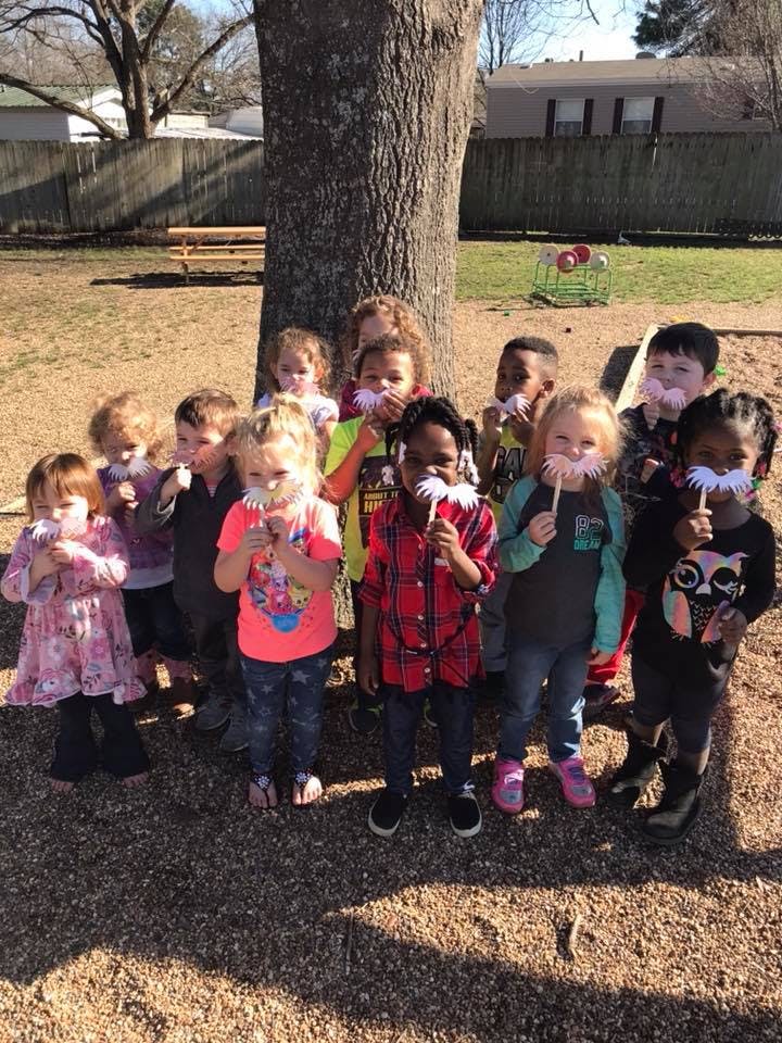 Group of children holding white paper mustaches in front of their faces