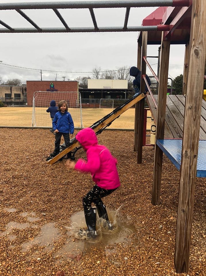 Child in pink jacket jumping in a puddle on a playground