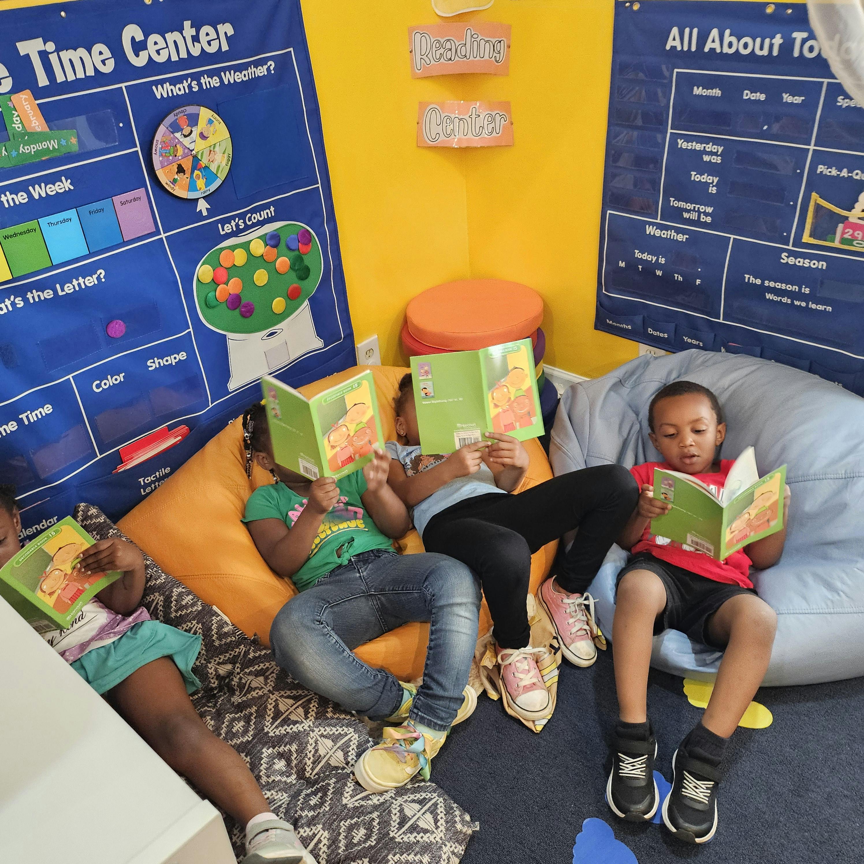 Four children reading books in a classroom