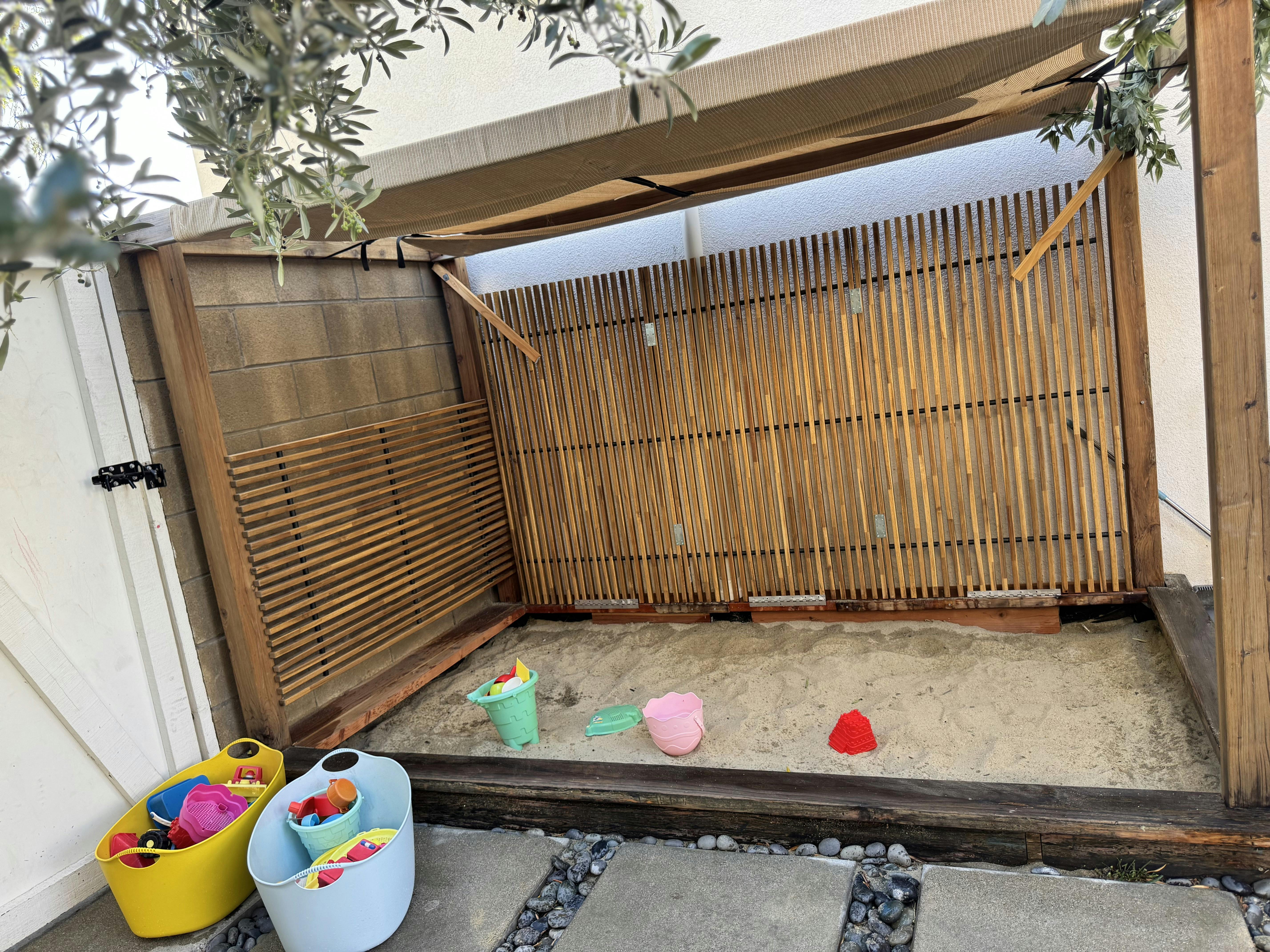 Sandbox with plastic toys and a wooden shade structure