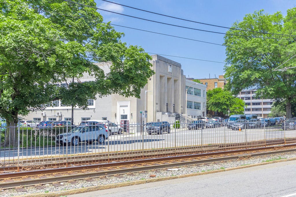 Building with columns and cars in a parking lot behind a fence and railroad tracks