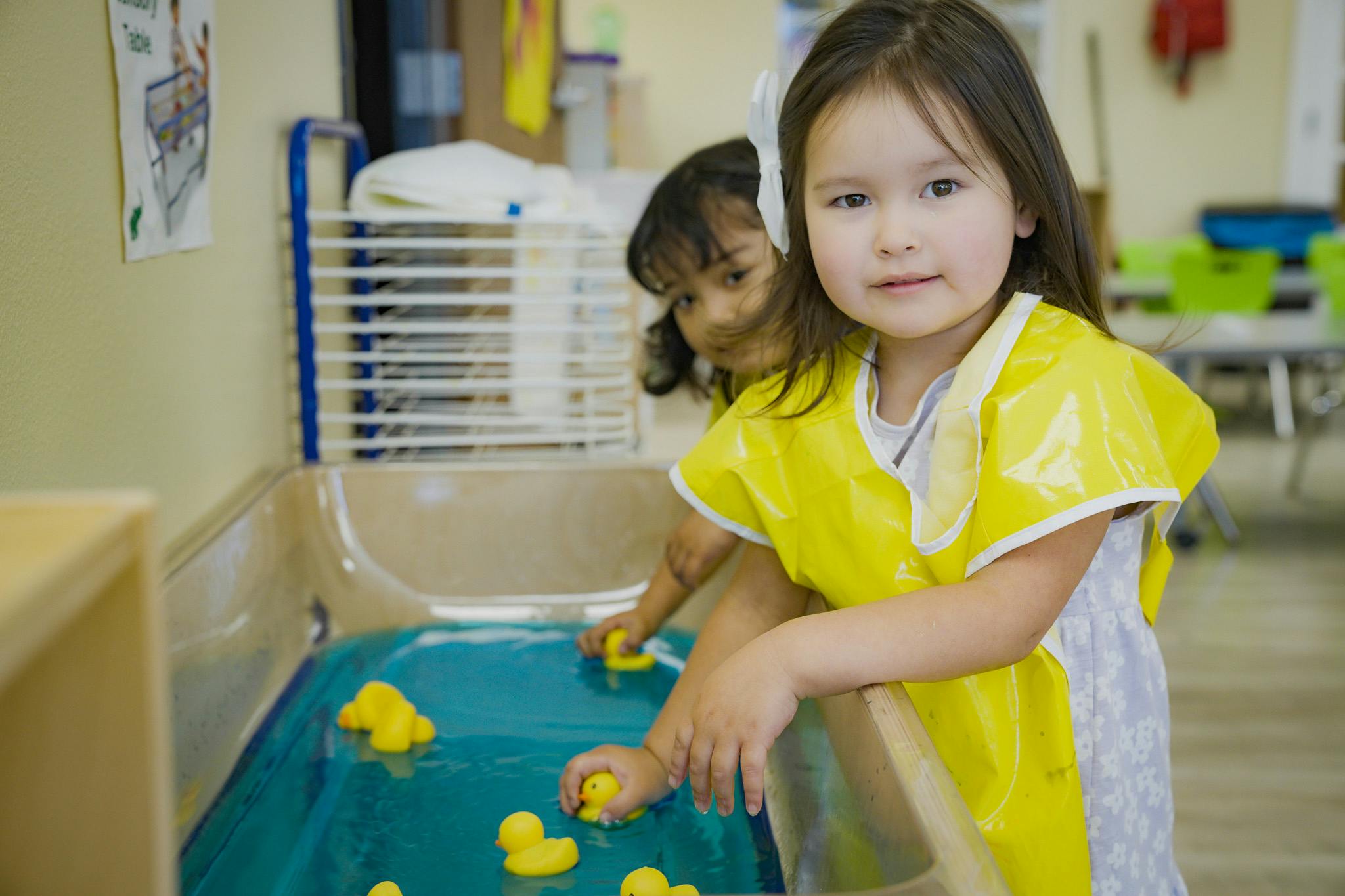 Two children playing with rubber ducks in a water table
