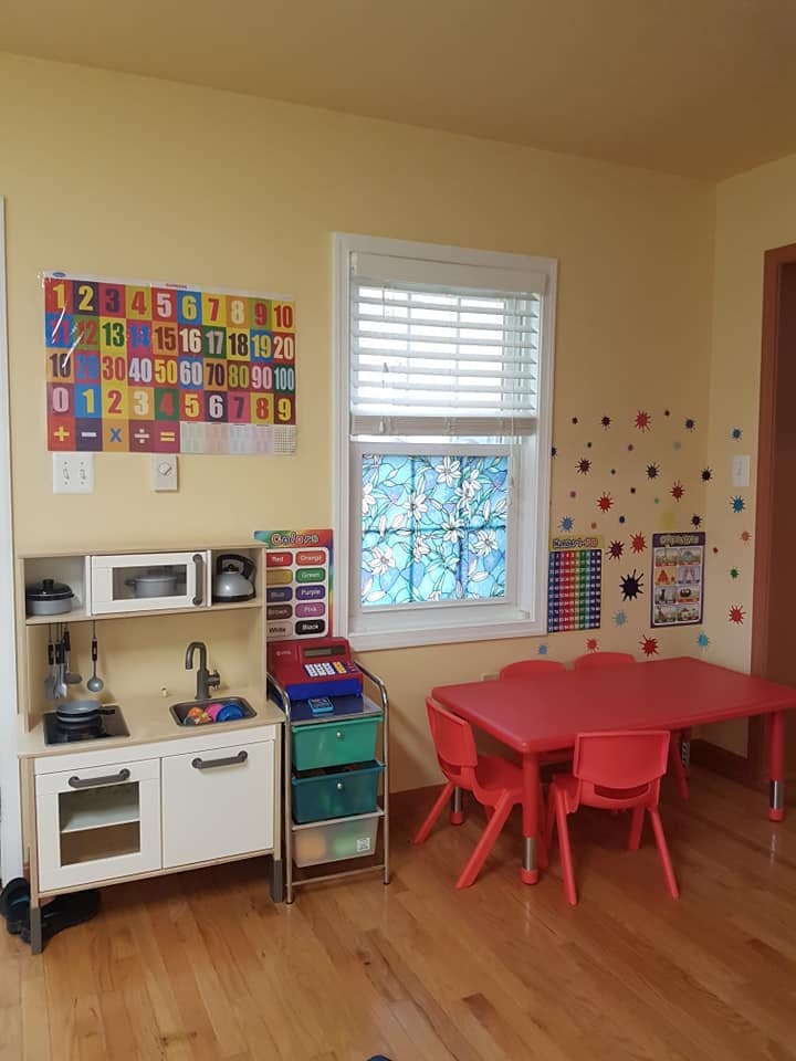 Play kitchen, red table and chairs, and number chart in a classroom