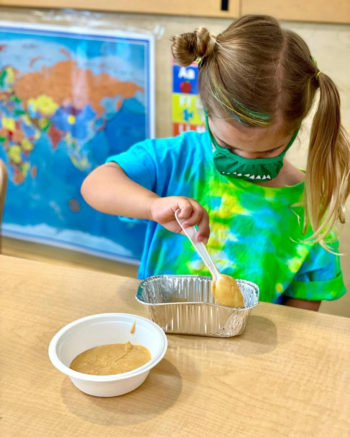 Child in a mask scooping a substance from a bowl into a foil container
