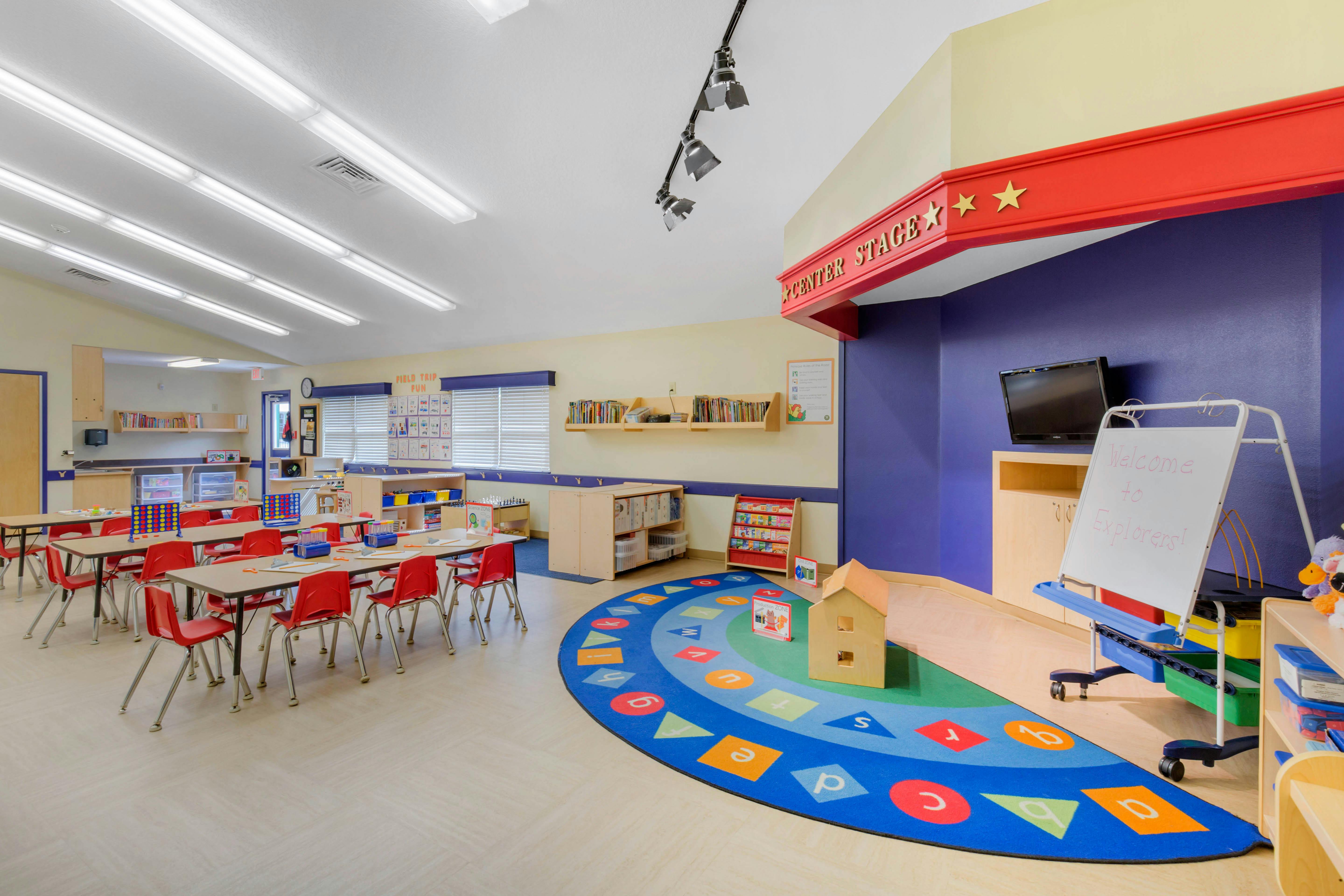 An empty classroom with desks and chairs, a play area with a rug, and a "Center Stage"