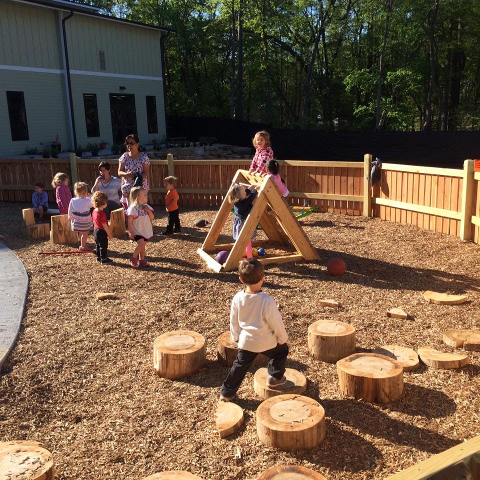 Children and adults on a playground with wood chips and tree stump steps