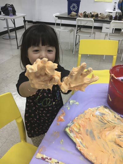 Child with hands covered in orange paint