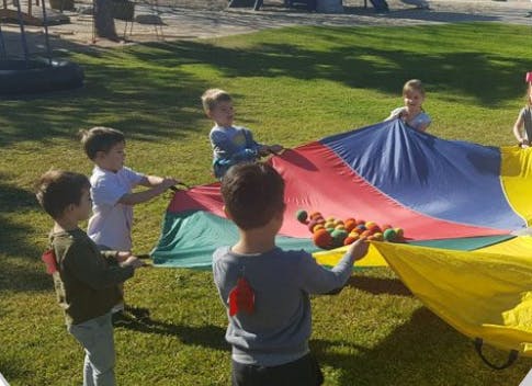 Children playing with a colorful parachute and small balls outdoors