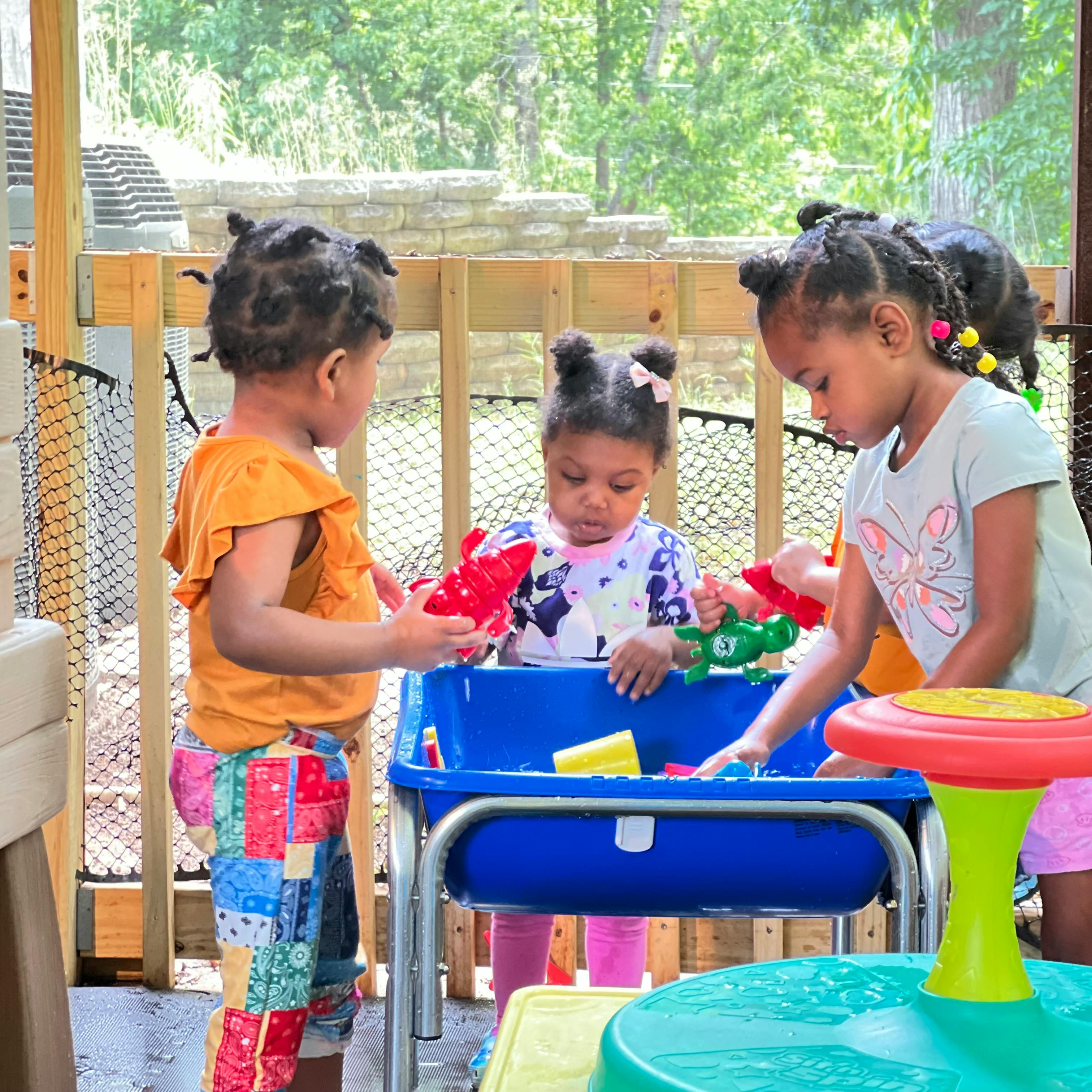 Three children playing with toys in a blue water table