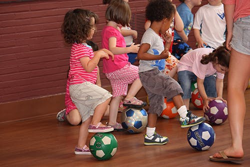 Children standing with one foot on soccer balls