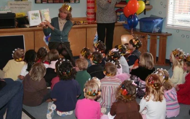 Person reading a book to a group of children sitting on the floor