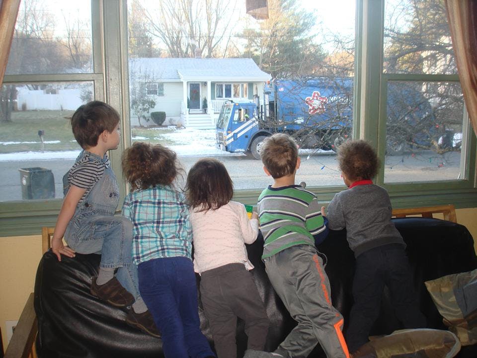 Four children looking out a window at a garbage truck