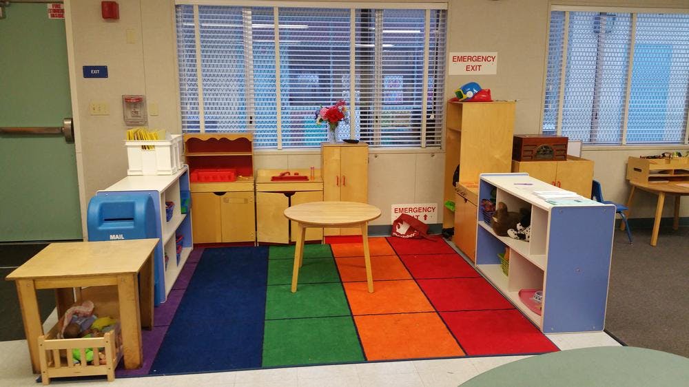 Classroom with small tables, chairs, and storage units on a colorful rug