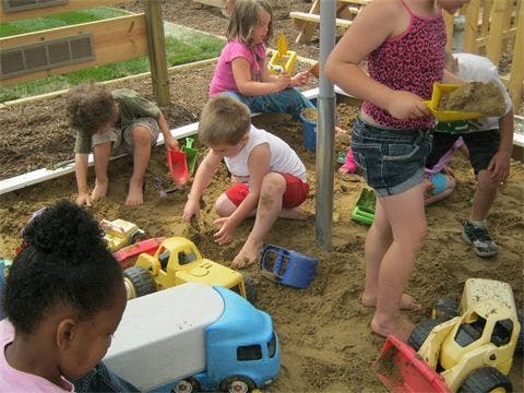 Children playing in a sandbox with toy trucks and shovels