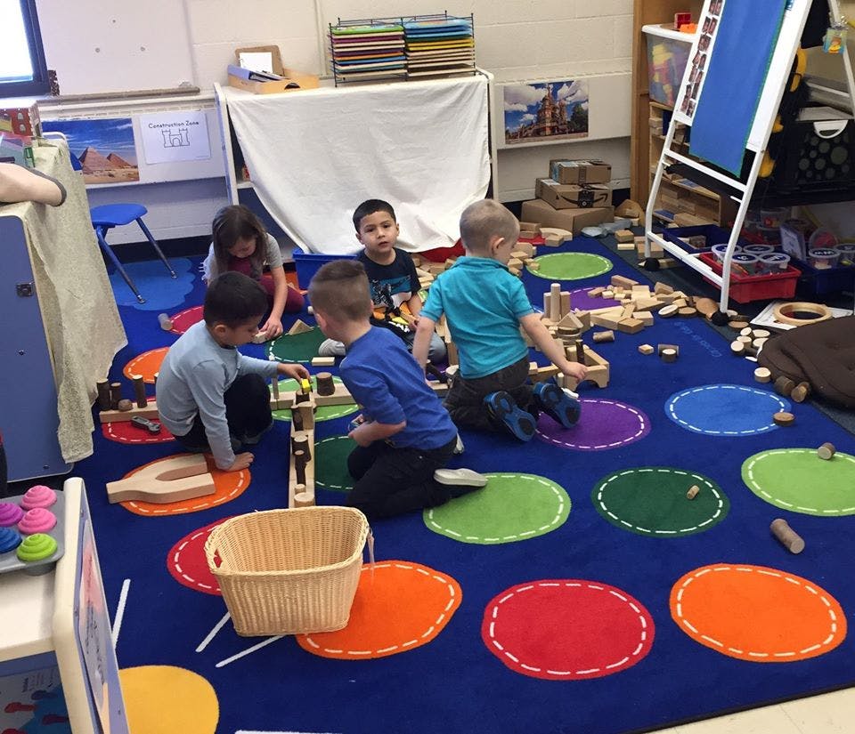 Children playing with wooden blocks on a colorful rug in a classroom