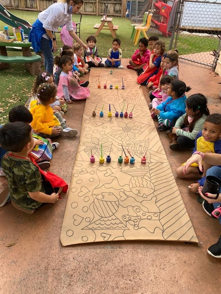 A group of children sitting around a large paper outline for a group art project