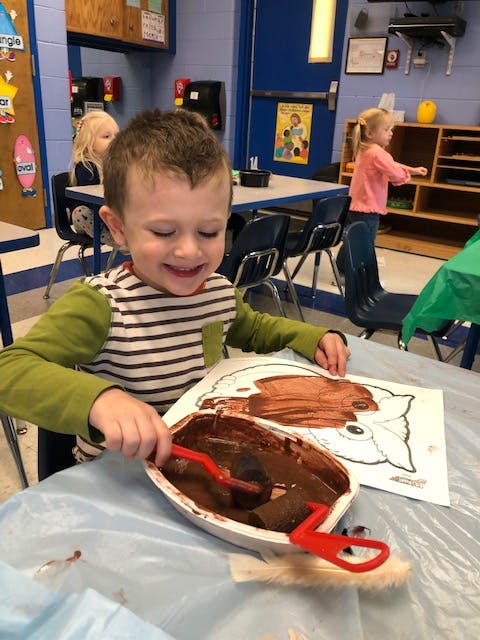 Child painting a picture with brown paint in a classroom