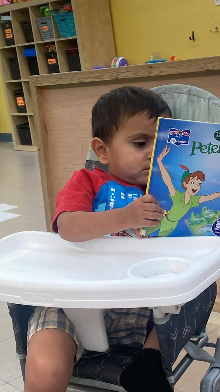 Child in a high chair holding a book with Peter Pan on the cover