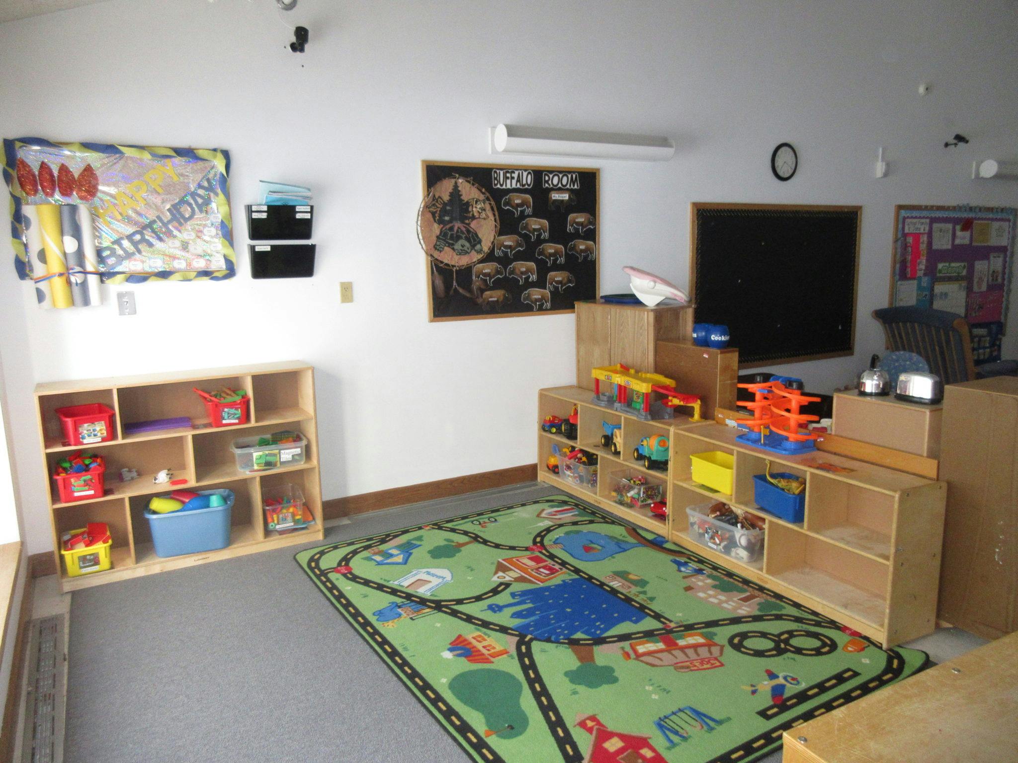 Playroom with toy shelves, a green rug with roads, and wall decorations