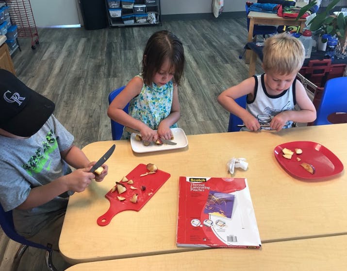 Three children cutting food at a table