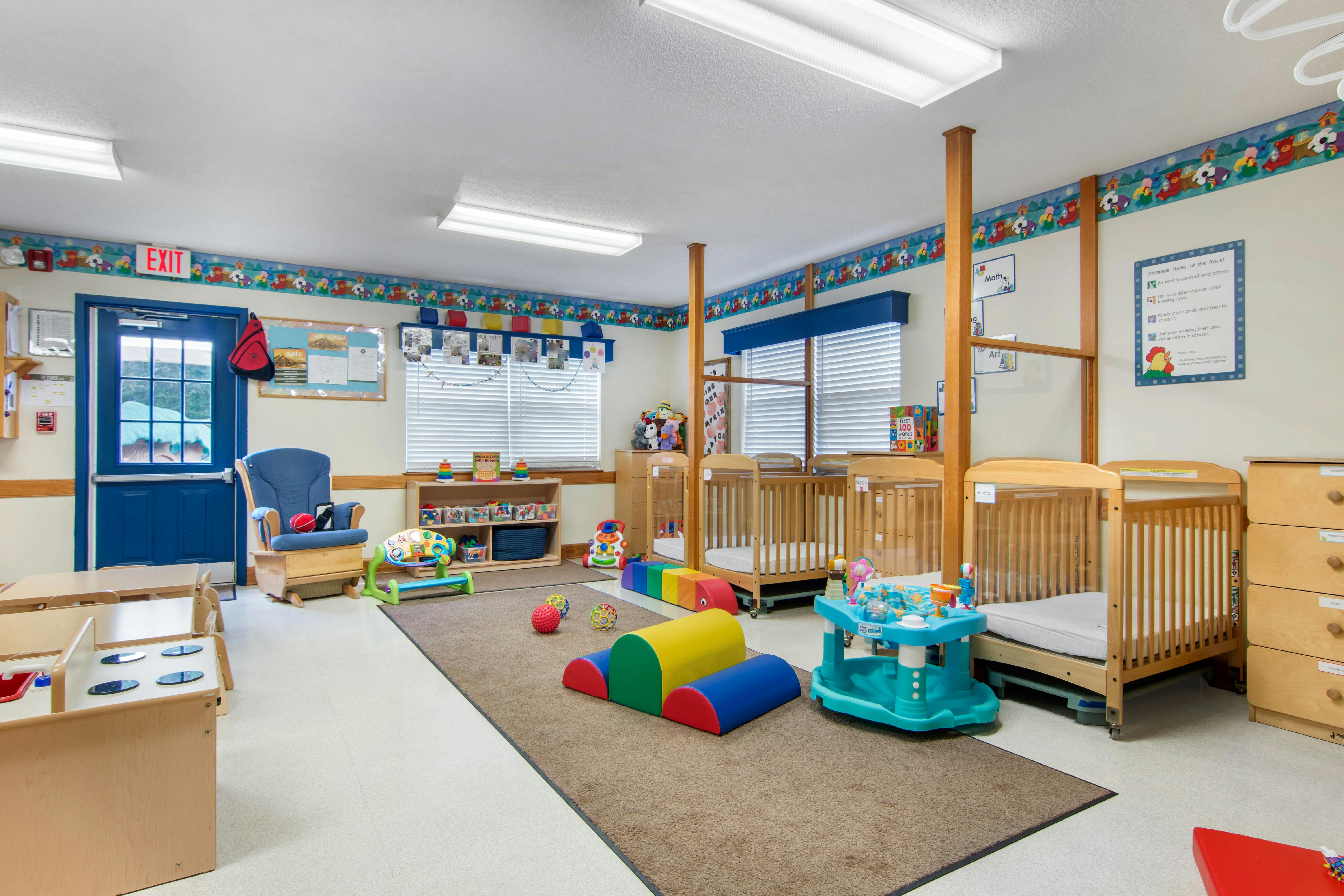 Classroom with multiple cribs, a rocking chair, child-sized furniture, and playmats