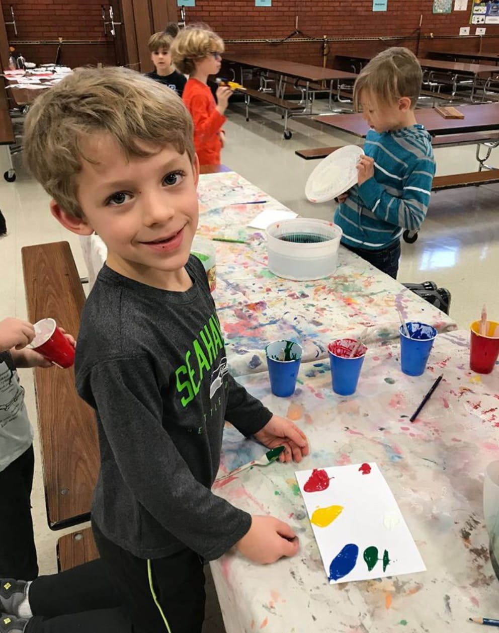 Child painting at a table with other children in the background