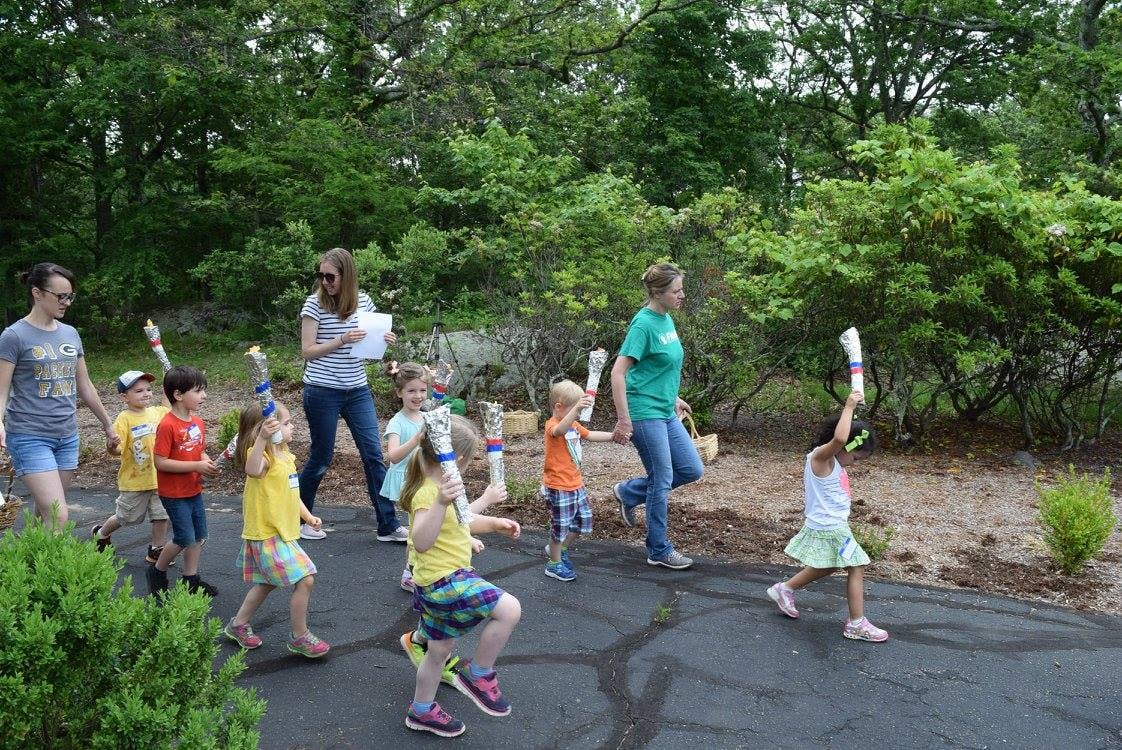 Adults and children walking outdoors, some holding up white objects