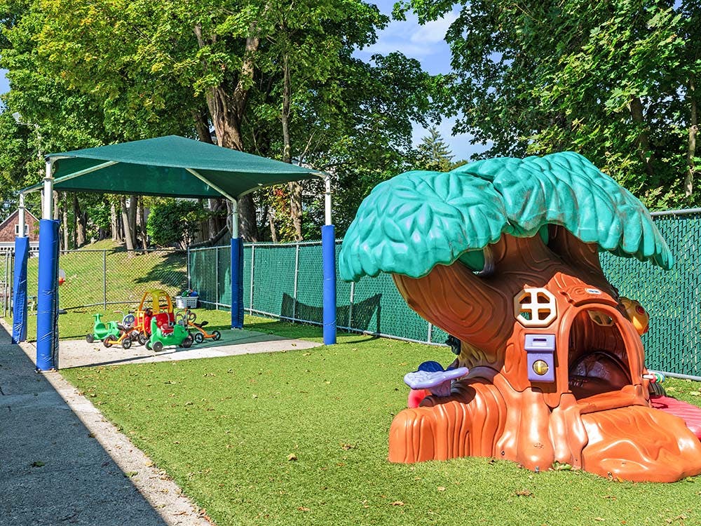 Playground with a shade structure, riding toys, and a tree-shaped playhouse