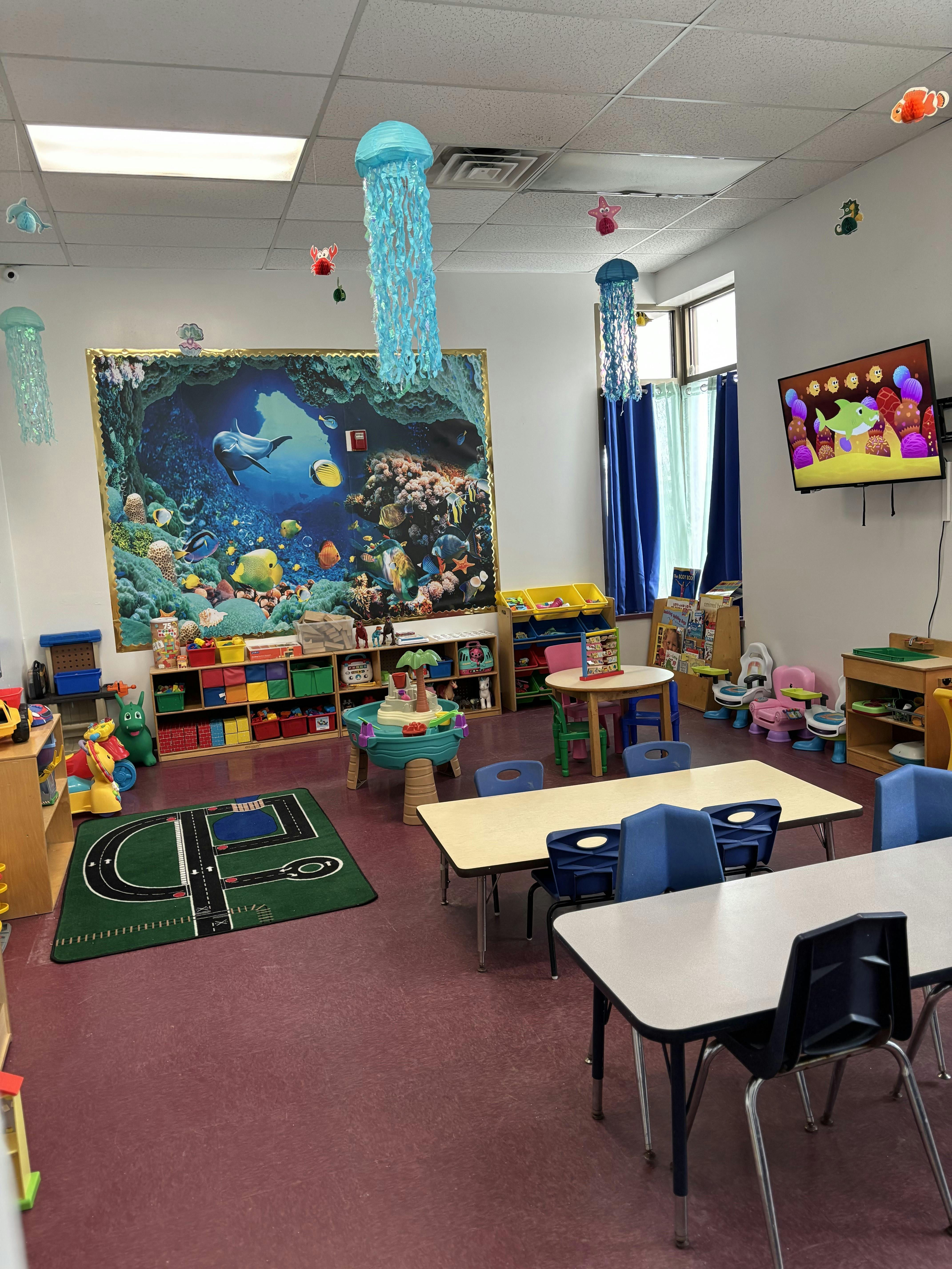 An empty children's classroom with small tables and chairs, toys, and an ocean-themed mural