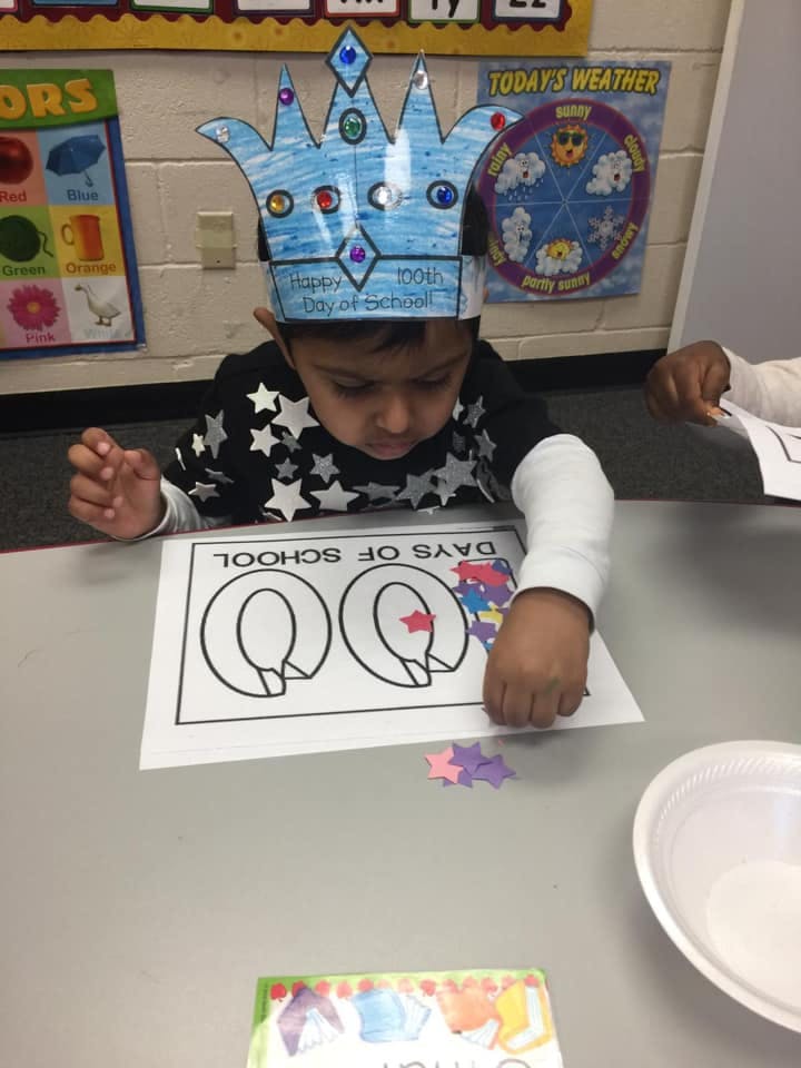 Child wearing a crown, placing star stickers on a paper with "100 DAYS OF SCHOOL"