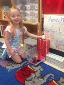 Child kneeling on a rug next to a whiteboard and red box