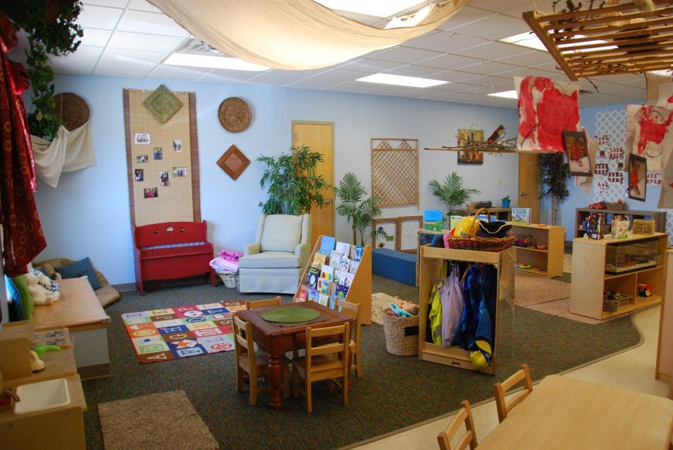 Classroom with small tables and chairs, shelves, and a colorful rug