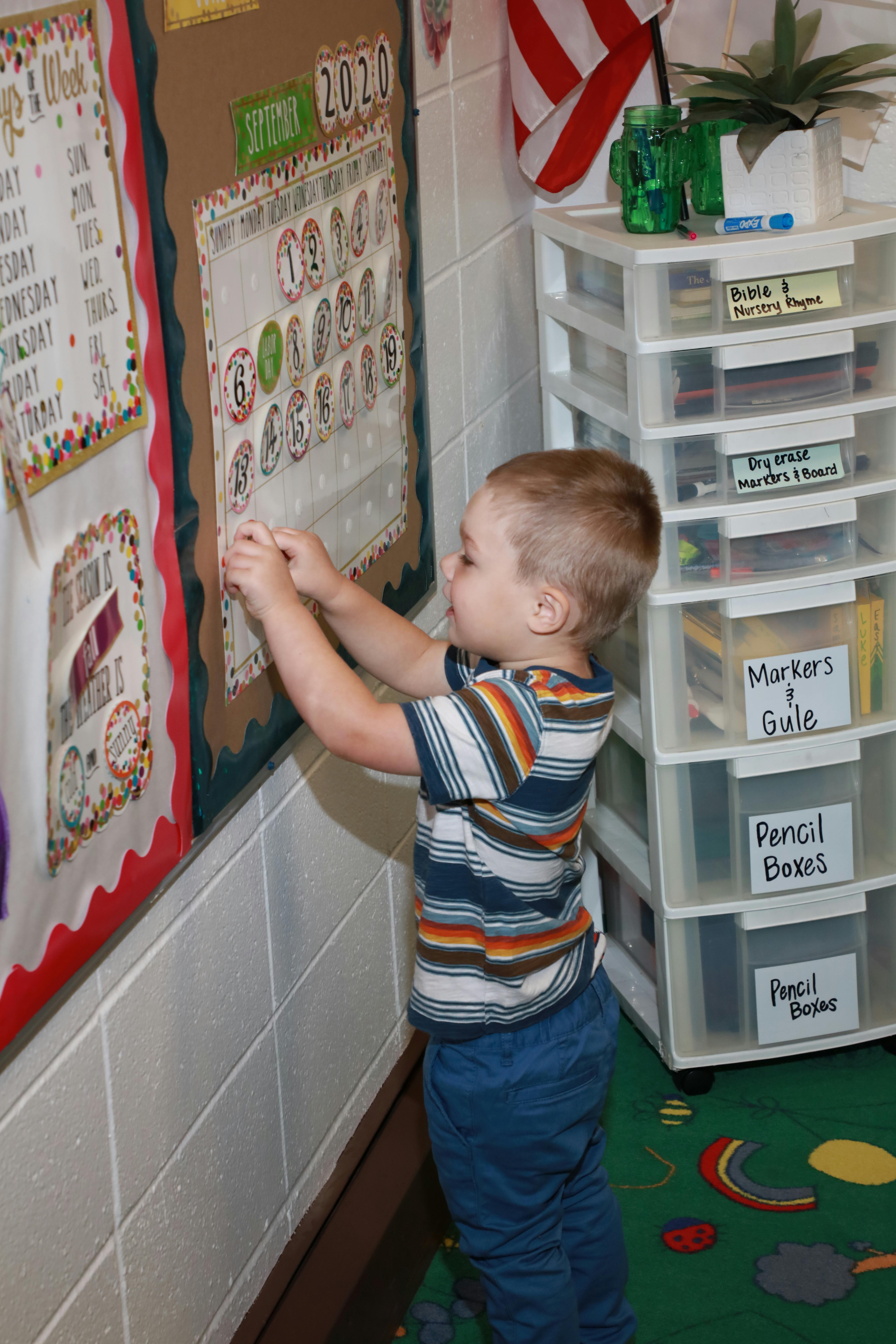 Child interacting with a calendar on a bulletin board in a classroom