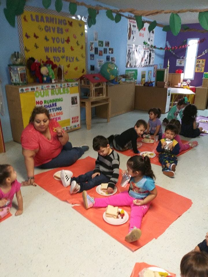 Adult and children sitting on floor eating in classroom eating snacks