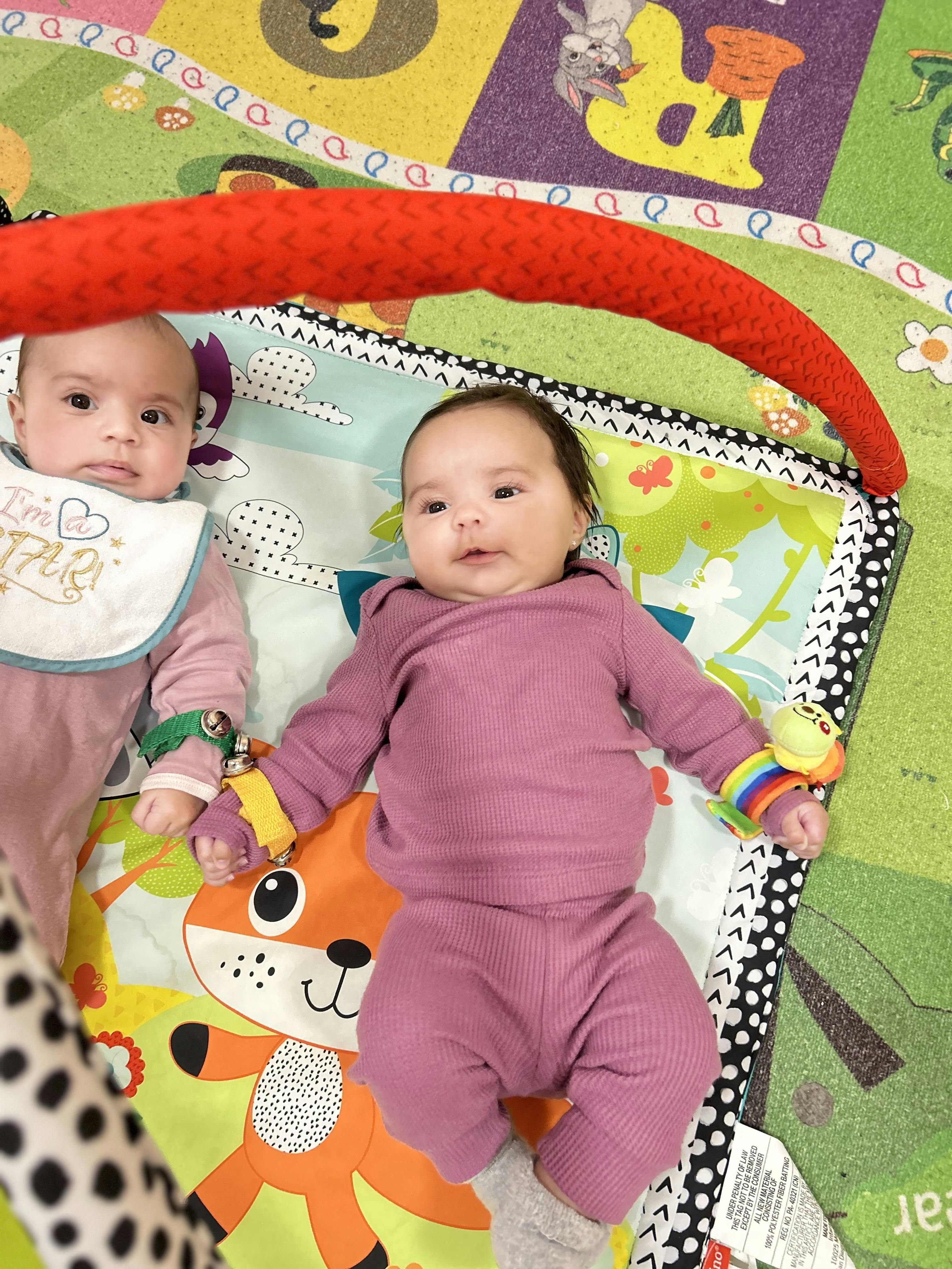 two babies lying on a playmat, one wearing a bib with "I'm a STAR!"