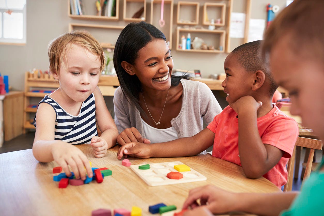 Adult and children playing with blocks at a table in a classroom