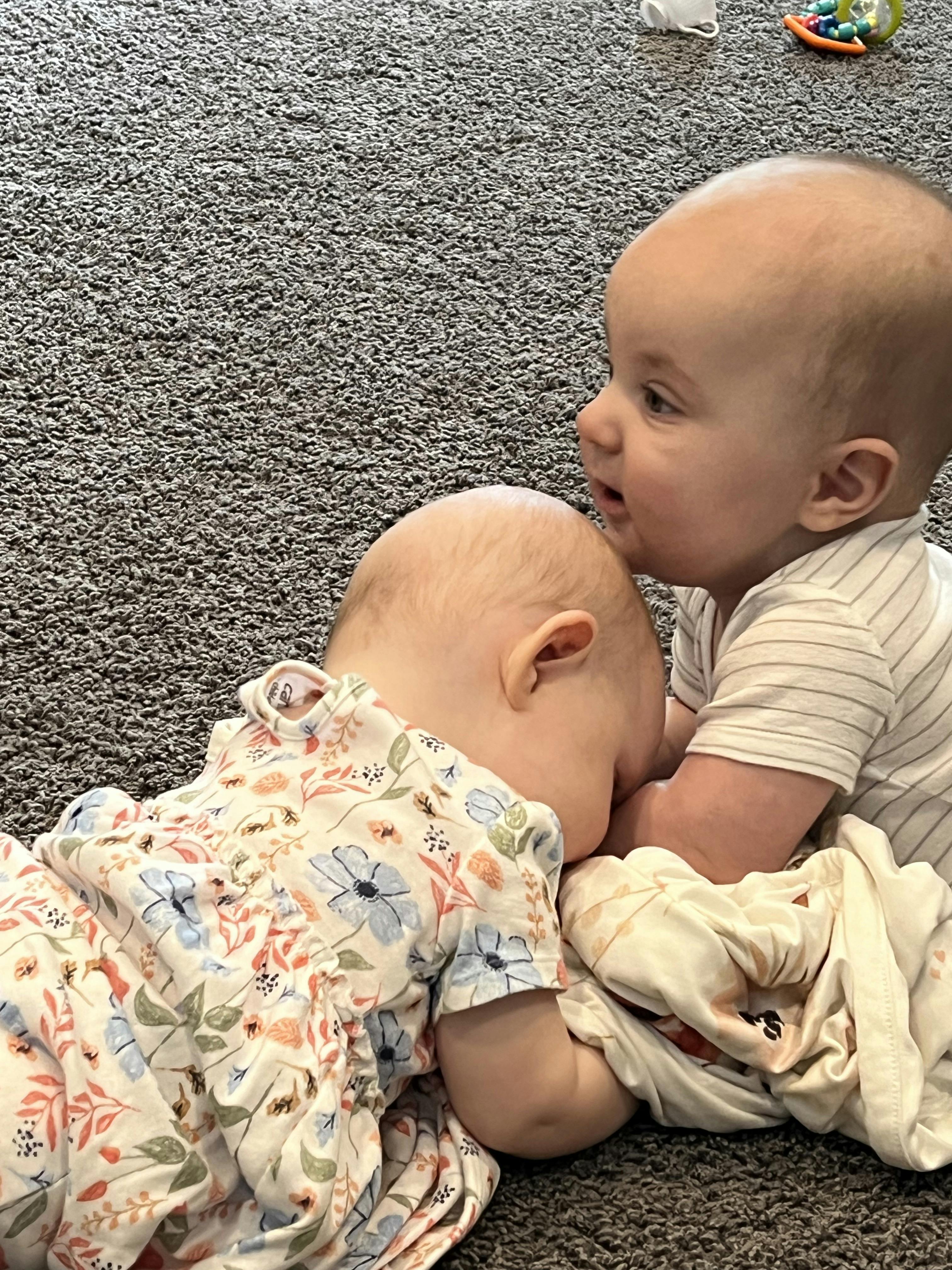 One baby looking at another baby resting its head on the floor