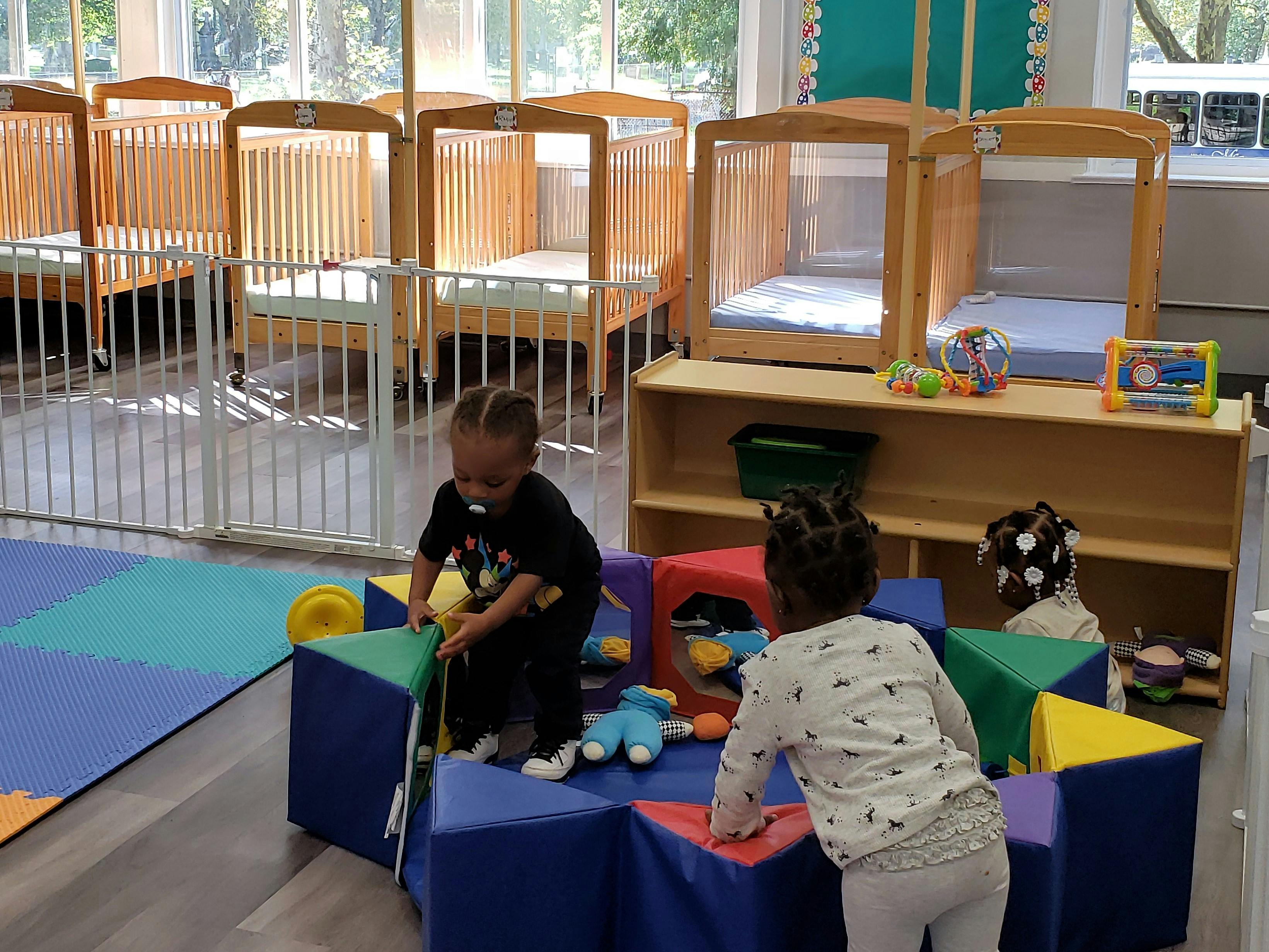 Two children playing with soft blocks in a room with cribs