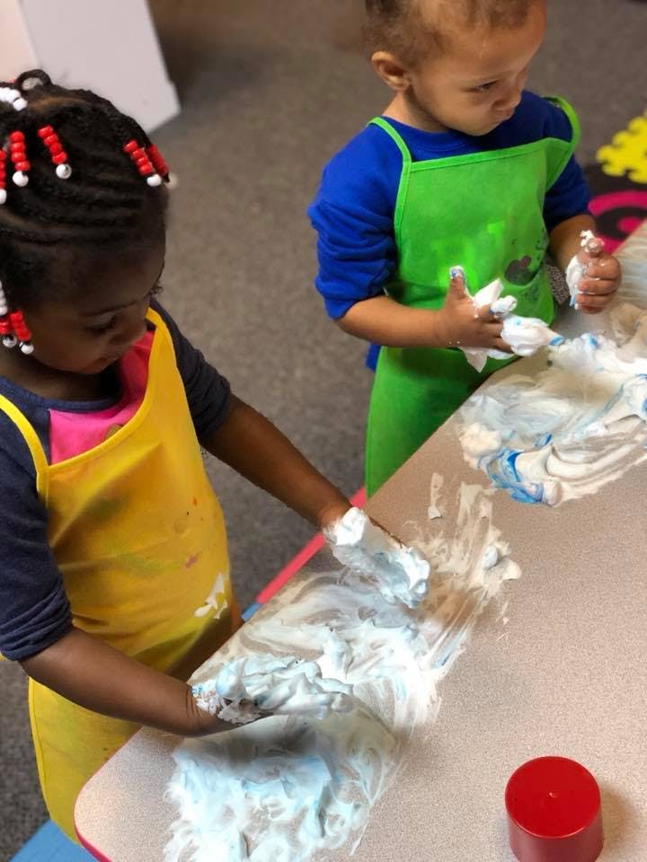 Two children playing with shaving cream on a table