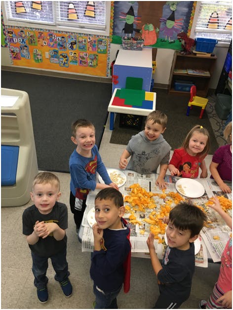 Children gathered around a table with pumpkin guts in a classroom