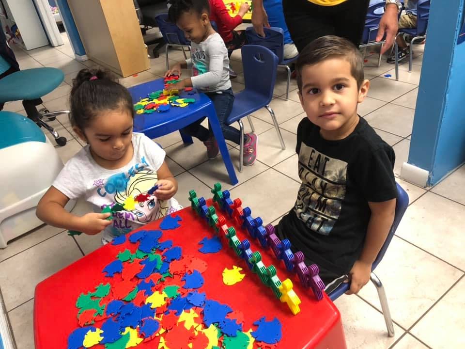 Two children playing with colorful puzzle pieces at a red table