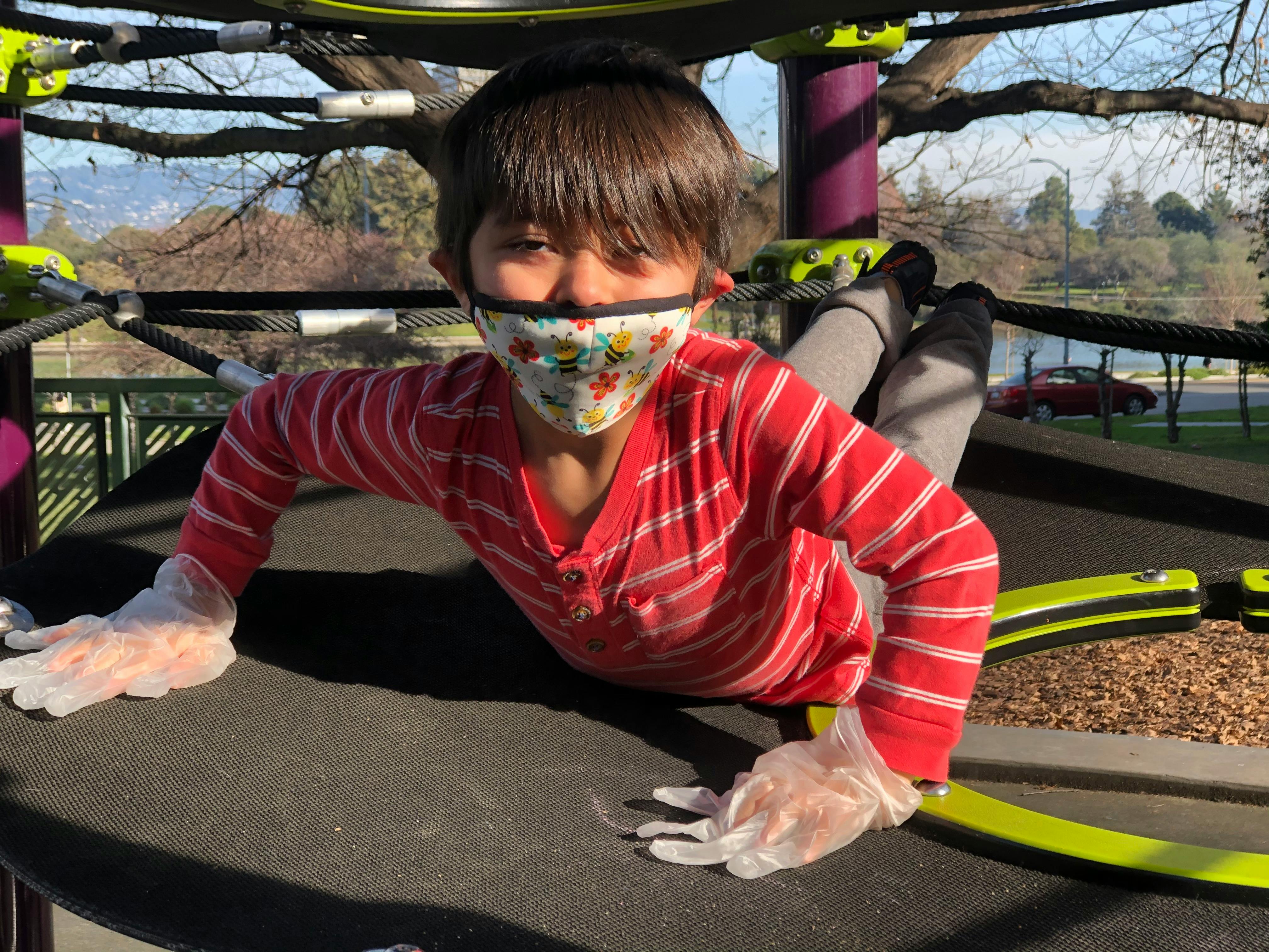 Child in a mask and gloves crawling on a playground structure