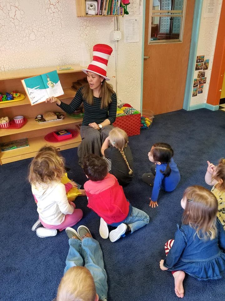 Person in striped hat reading a book to children in a classroom