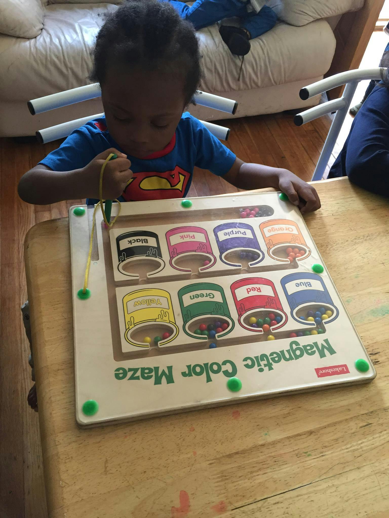 Child playing with a magnetic color maze toy on a wooden table