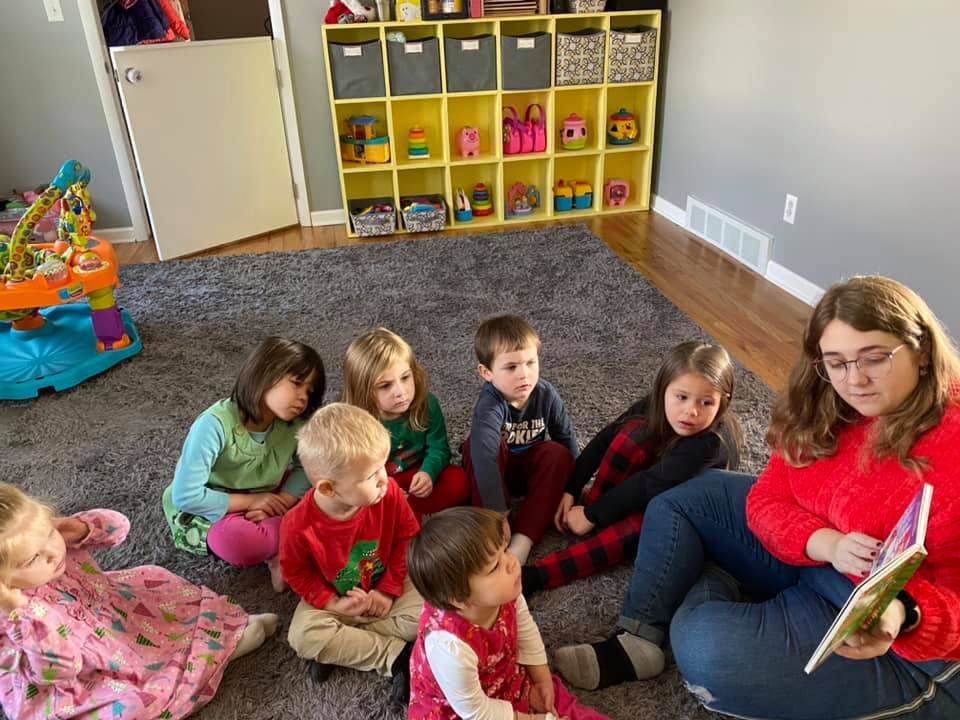 Person reading a book to a group of children on a rug