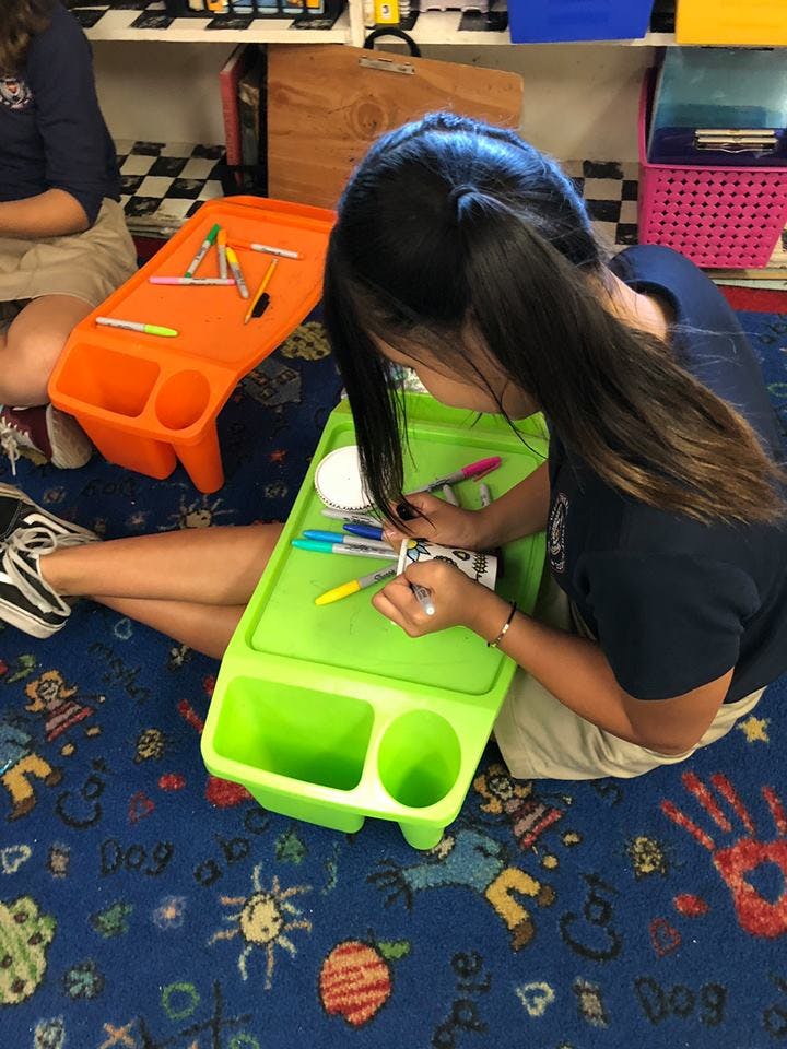 Child sitting on floor coloring with markers on a green lap desk
