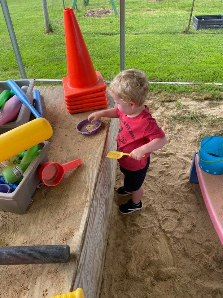 Child playing in a sandbox with a small shovel and bowl