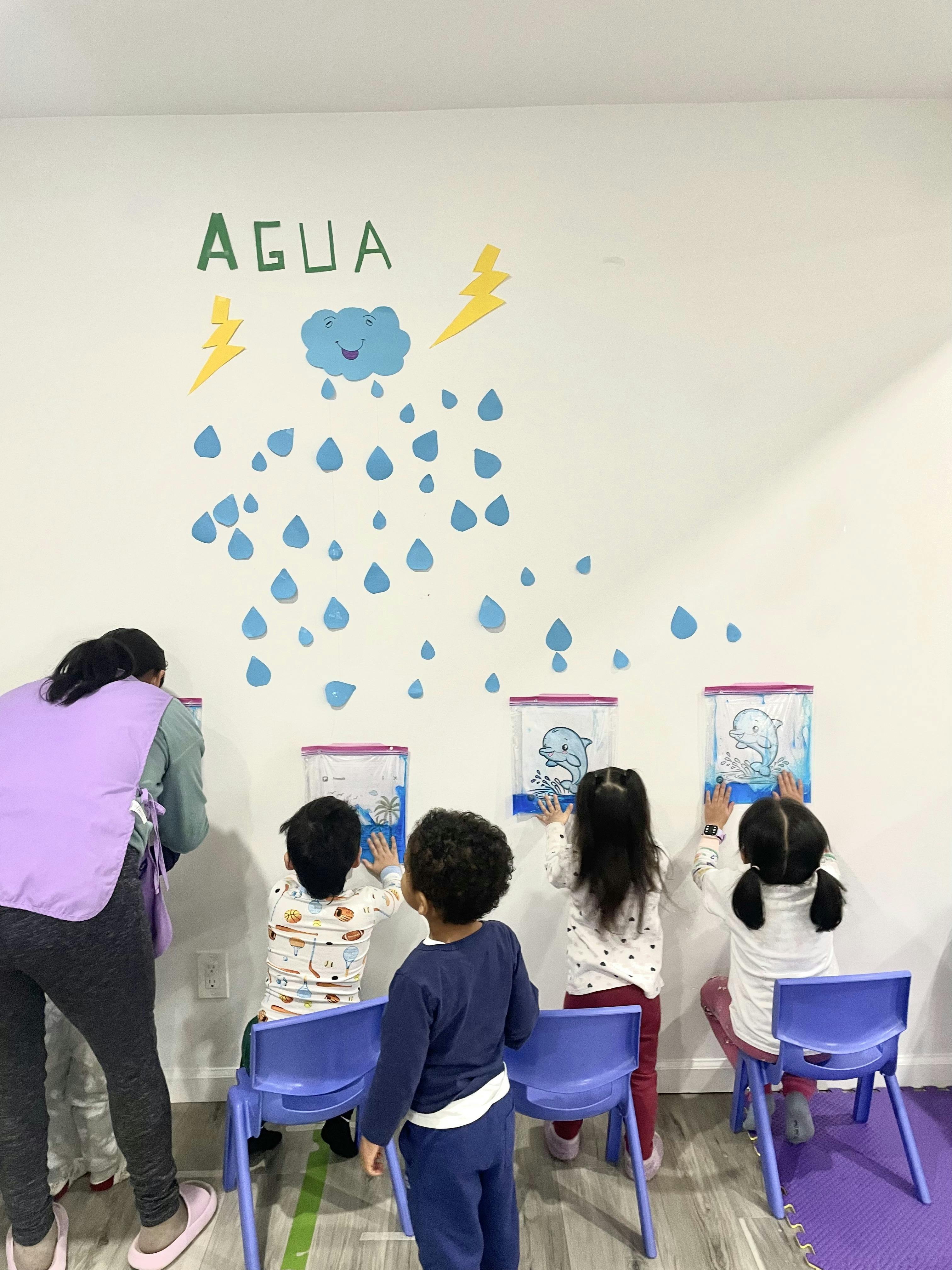 Adult and three children interacting with wall-mounted water activities in a classroom